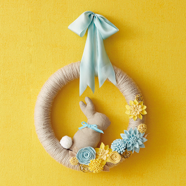 Twine wrapped wreath embellished with blue and yellow felt flowers, a blue bow, and a fabric easter bunny.