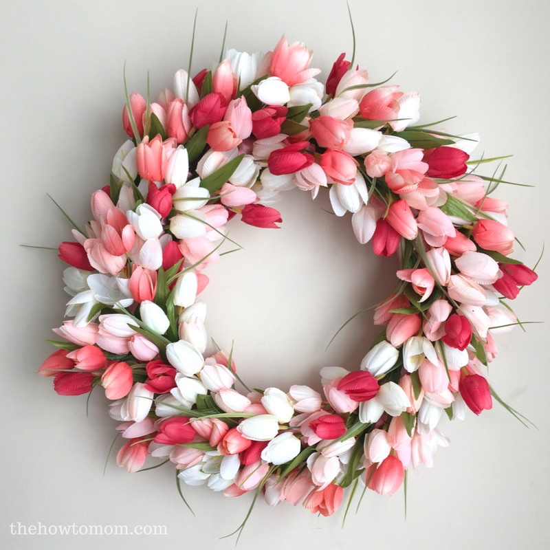 red, pink, and white silk tulip flowers arranged into a wreath for spring, on a white surface.