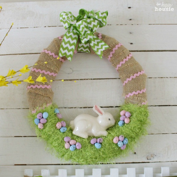 Easter wreath wrapped with burlap and fuzzy green yarn that looks like grass.  Easter eggs and an easter bunny set on the grassy part.
