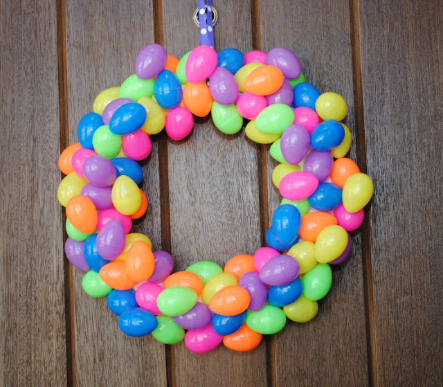 Wreath made of colorful plastic easter eggs hanging on a dark wood surface.