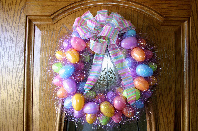 Colorful Easter egg wreath made with pink easter grass, topped with a big striped bow, on a brown door.