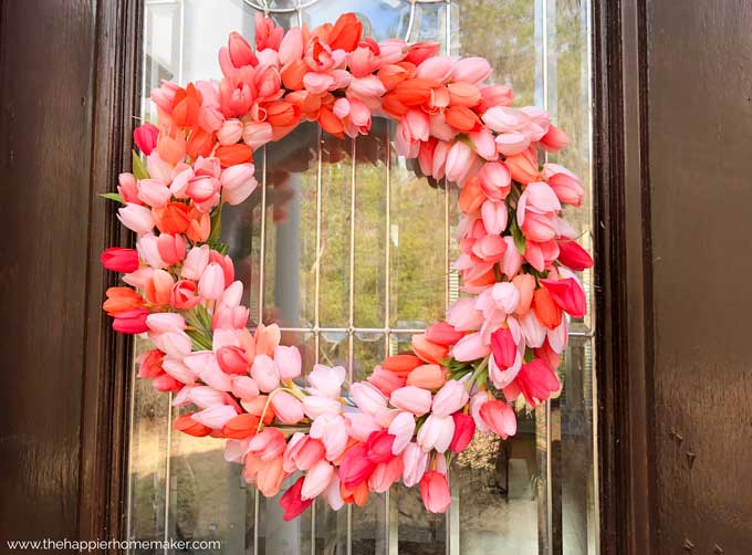 artificial tulip wreath on a brown and glass front door.