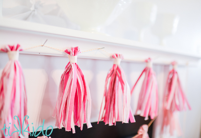 Pink paper tassel garland on a white fireplace mantle.